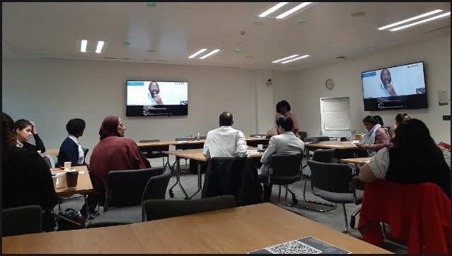 ICDP alumni and participants sitting around tables watching the keynote speaker Terry Roberts on a screen on the wall
