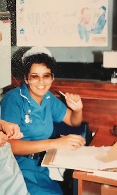 Sharon Hodsgon, wearing a blue nurse's uniform and a white hat, sitting down at a desk.