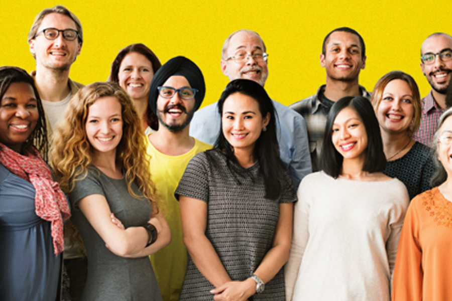 A group of men and women standing in a group smiling at the camera against a yellow background.