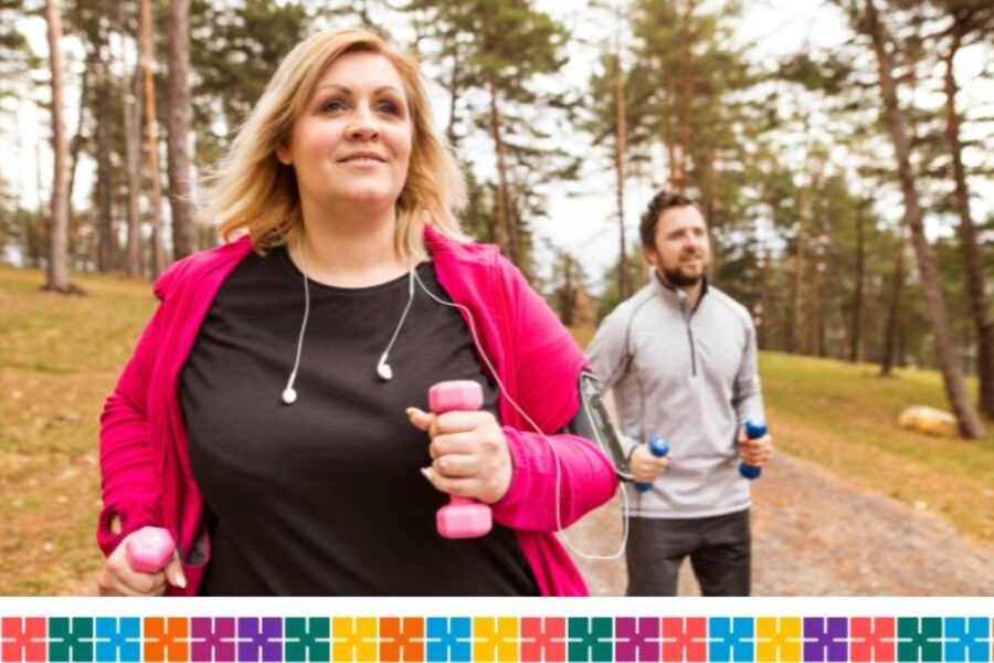 A woman wearing exercise top and hoodie and holding dumb bells running in a park with a man