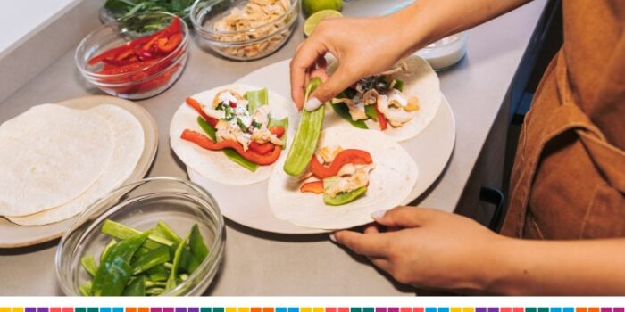 Someone is making tacos on a kitchen worktop with bowls of tortilla and vegetables laid out in different bowls.