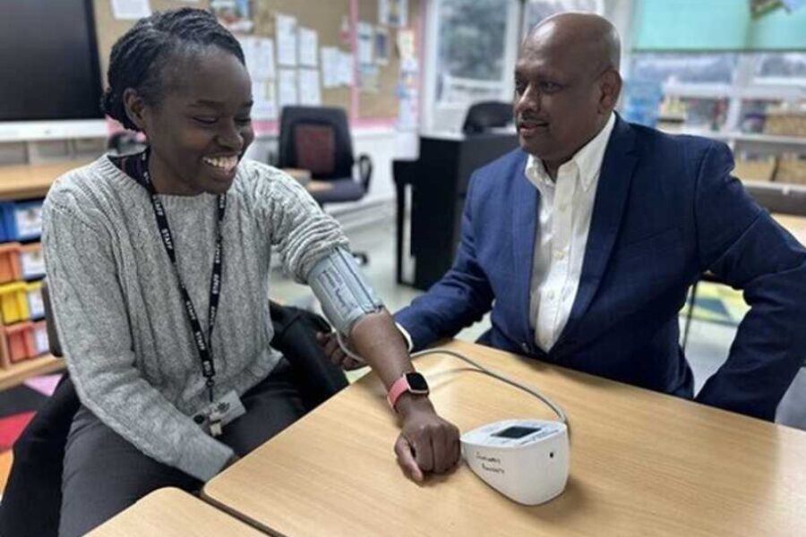 Young woman and man sitting at a table. Woman has a blood pressure cuff on her arm as her blood pressure is being checked