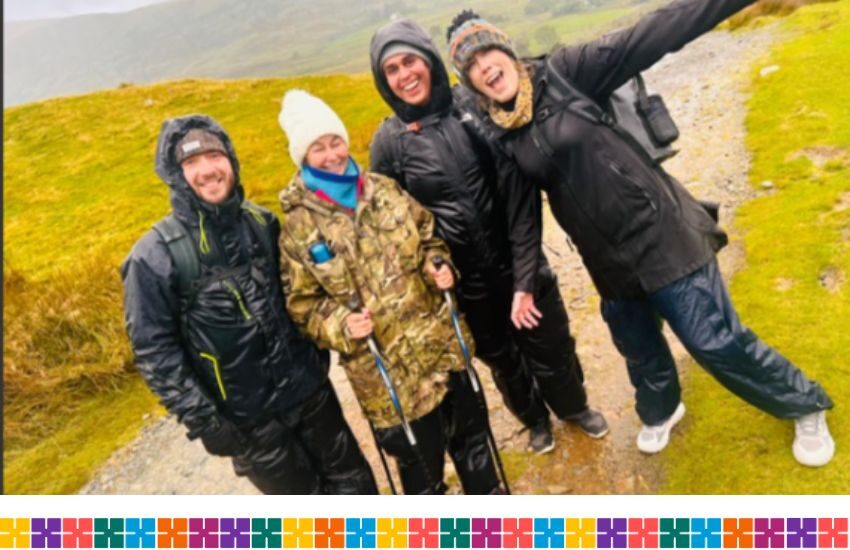 A group of smiling people who are outside on a walk up a mountain