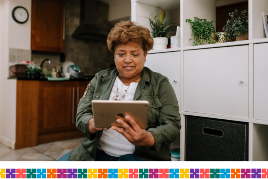 Person sitting in their living room with kitchen in the background. They are doing something on their iPad.