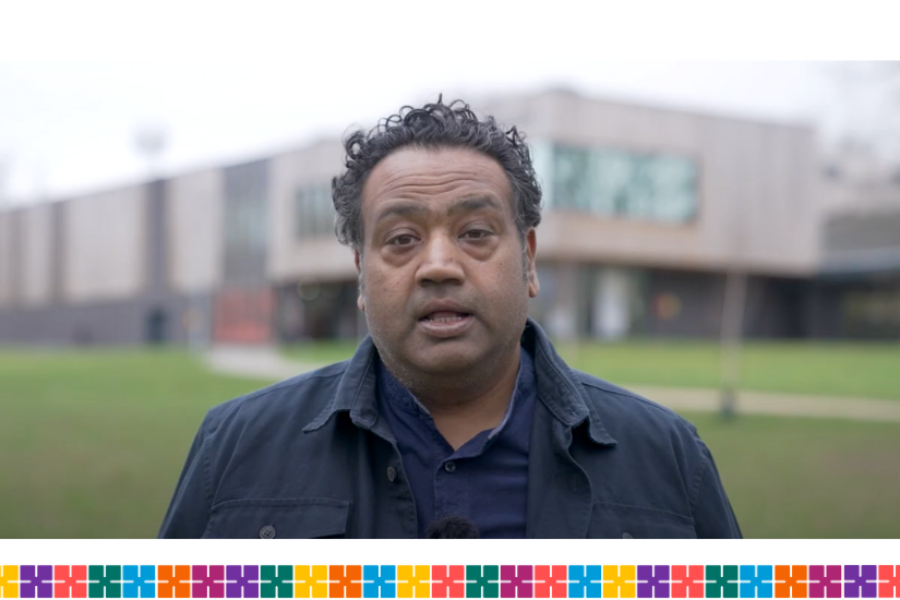 A man looking directly at the camera. He is outdoors with an office building in the background.