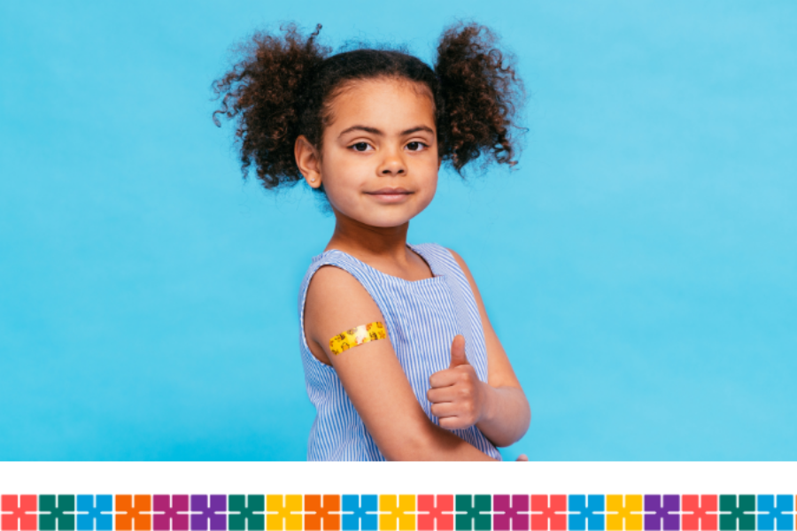 Young girl looking at the camera with her thumb up. She has a yellow plaster on her arm.